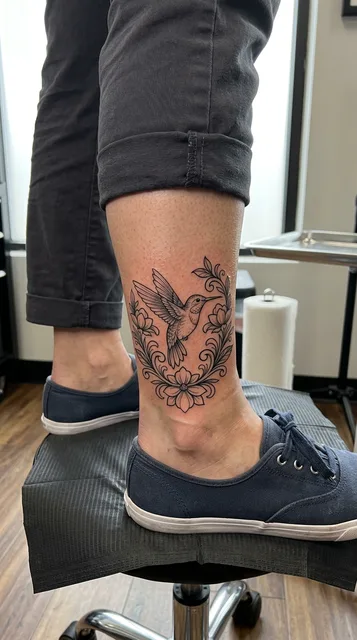 Black and grey ornamental hummingbird tattoo on a woman's ankle