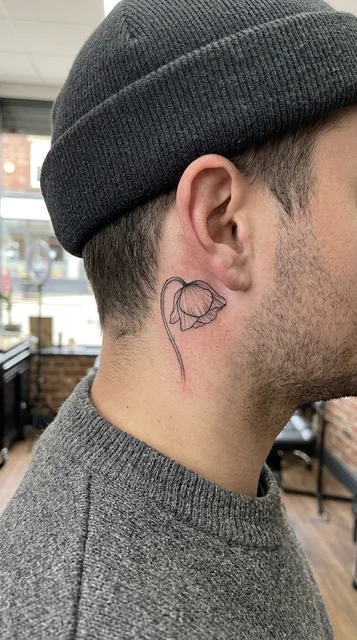 Black and white fine line flower tattoo behind a man's ear