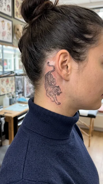 Black and white fine line tiger tattoo behind a woman's ear