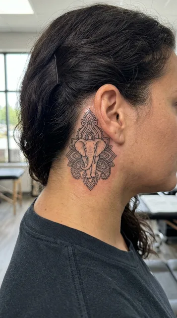 Black and grey illustrative elephant tattoo behind a woman's ear