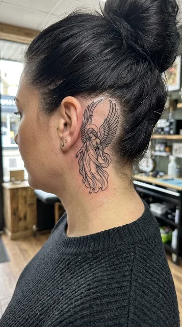 Black and white linework angel tattoo behind a woman's ear