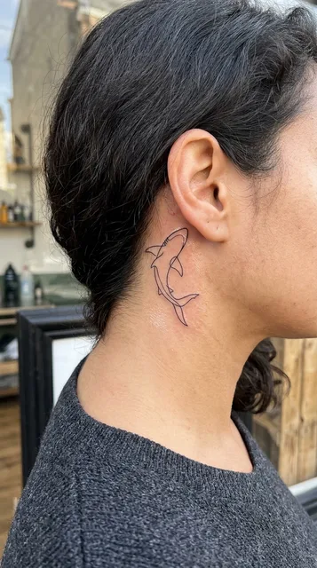 Black and white linework shark tattoo behind a woman's ear