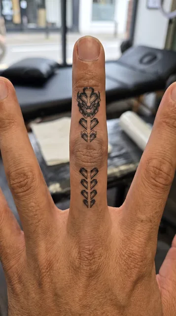 Black and grey biomechanical robot mask tattoo on a man's finger