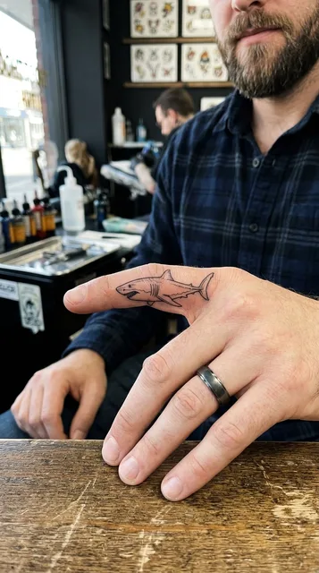 Black and white fine line shark tattoo on a man's finger