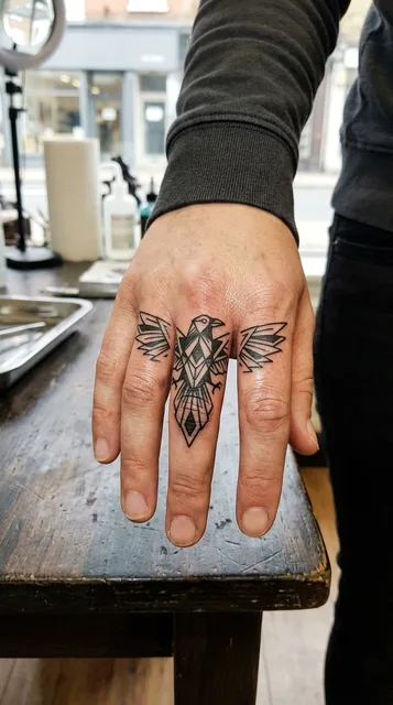 Black and white geometric raven tattoo on a woman's finger