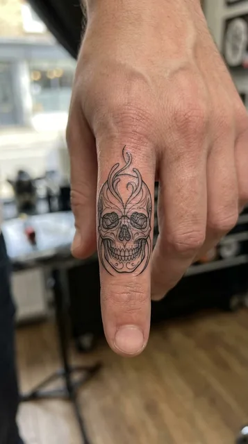 Black and white linework skull tattoo on a man's finger
