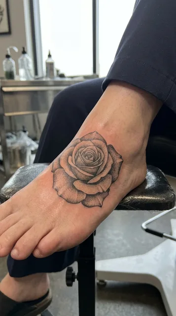 Black and grey dotwork rose tattoo on a woman's foot