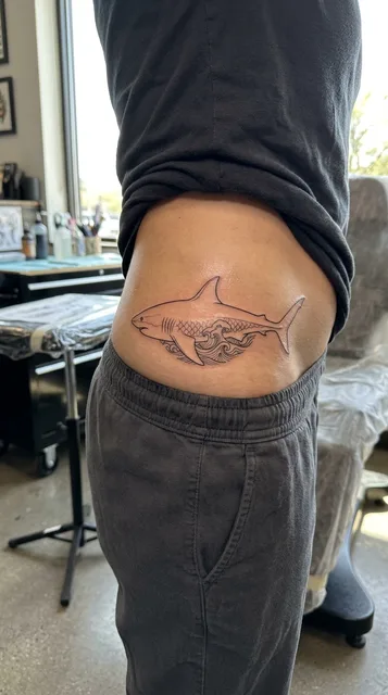 Black and white fine line shark tattoo on a woman's hip