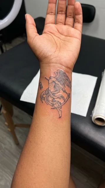 Black and grey illustrative angel tattoo on a woman's wrist