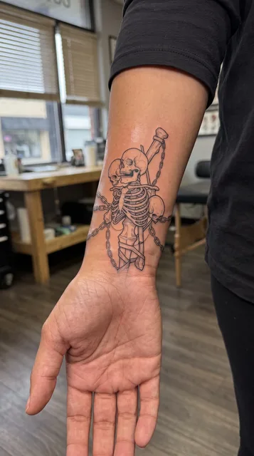 Black and grey illustrative skeletons tattoo on a woman's wrist
